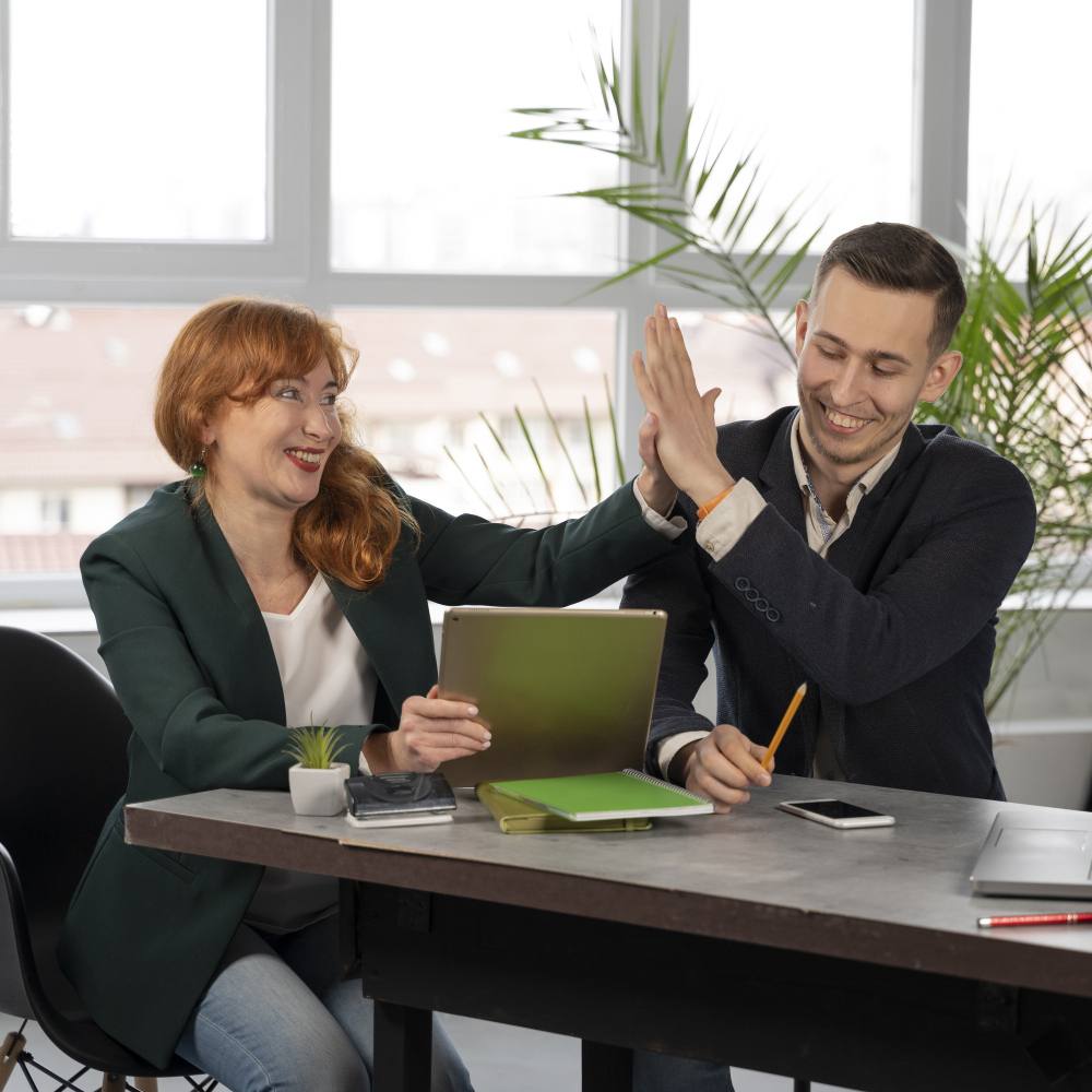 Two professionals collaborating in a modern office, one holding a tablet and the other giving a high five.